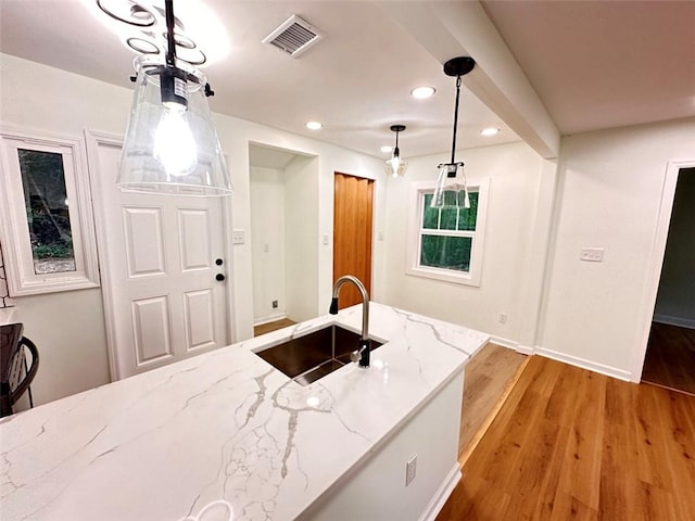 kitchen with light stone countertops, hanging light fixtures, light hardwood / wood-style flooring, and sink