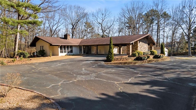 view of front facade with driveway, stone siding, a chimney, a carport, and stucco siding