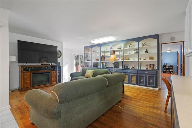living area with built in shelves, a fireplace, and wood finished floors