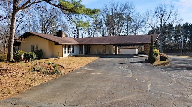 single story home with aphalt driveway, an attached carport, a chimney, and stucco siding