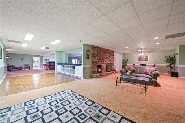 living room featuring wainscoting, carpet flooring, a fireplace, and a drop ceiling