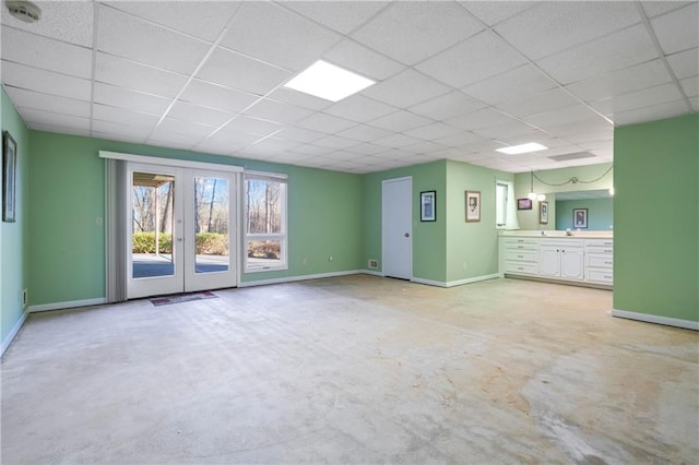 interior space featuring french doors, a drop ceiling, baseboards, and unfinished concrete floors