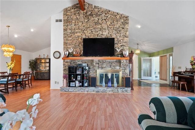 living area with a chandelier, a stone fireplace, lofted ceiling with beams, and wood finished floors