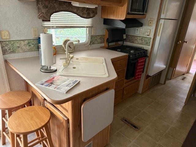 kitchen with visible vents, wallpapered walls, light countertops, a sink, and gas stove