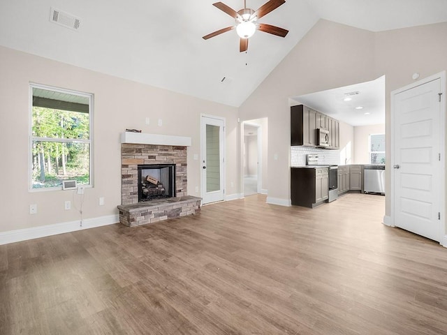 unfurnished living room featuring visible vents, a fireplace with raised hearth, light wood-style flooring, ceiling fan, and high vaulted ceiling