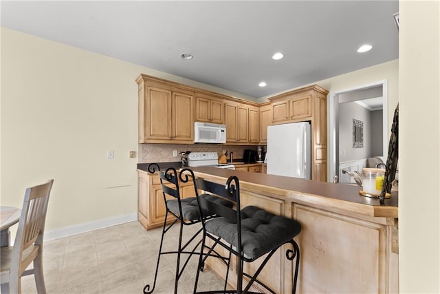 kitchen with recessed lighting, white appliances, a kitchen breakfast bar, light brown cabinetry, and tasteful backsplash