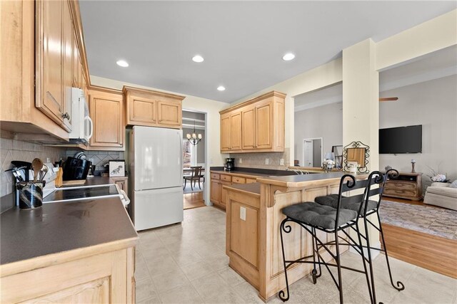 kitchen with a breakfast bar area, a peninsula, white appliances, open floor plan, and light brown cabinetry