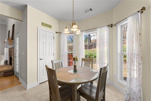 dining area featuring light tile patterned floors, baseboards, visible vents, an inviting chandelier, and a brick fireplace