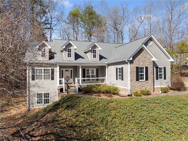 cape cod-style house with covered porch, stone siding, and a front yard