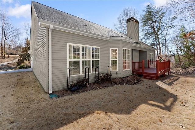 back of house featuring a shingled roof, a chimney, and a wooden deck