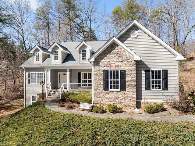 cape cod-style house featuring stone siding, a front lawn, and a porch