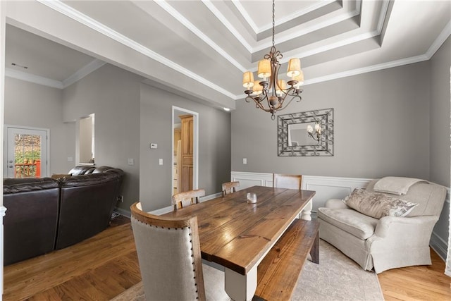 dining space with a chandelier, a tray ceiling, crown molding, and wood finished floors