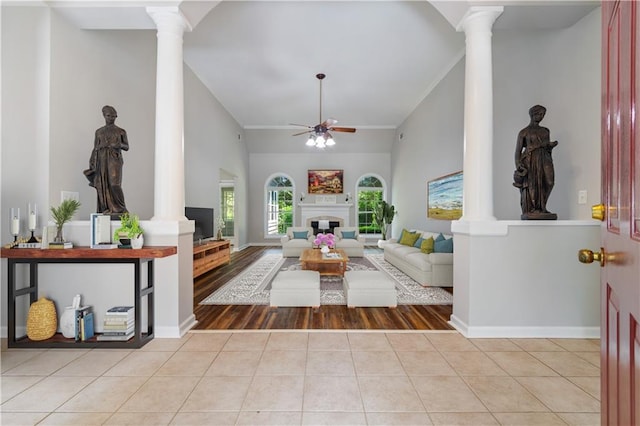 living area with a fireplace, decorative columns, light tile patterned floors, a ceiling fan, and ornamental molding