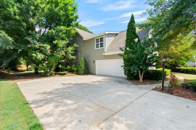 view of side of home with a garage, concrete driveway, and roof with shingles