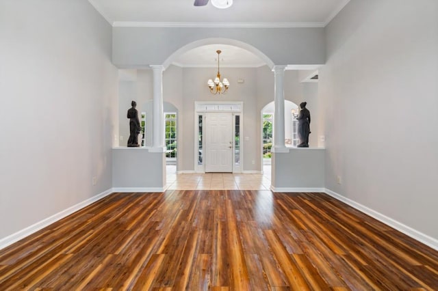 entryway with baseboards, arched walkways, wood finished floors, an inviting chandelier, and crown molding