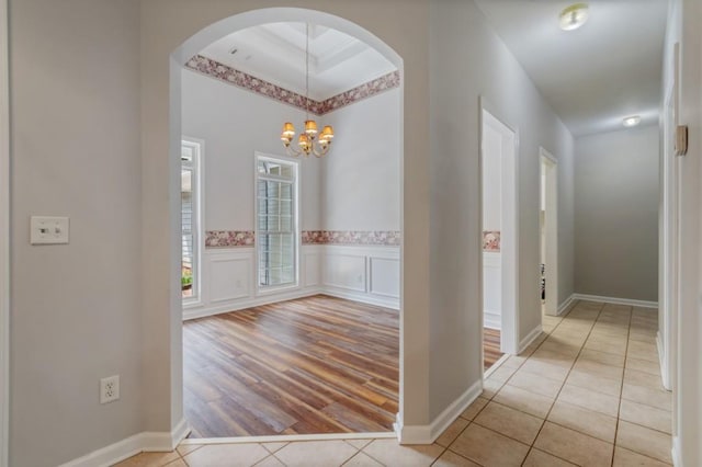 hallway with arched walkways, a decorative wall, wainscoting, light tile patterned flooring, and a chandelier