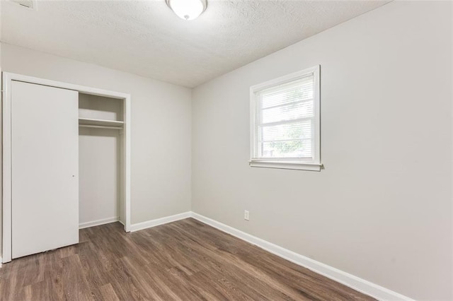 unfurnished bedroom with a textured ceiling, wood finished floors, a closet, and baseboards