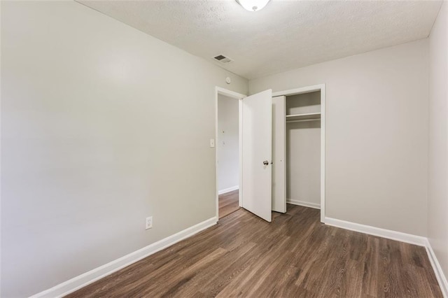 unfurnished bedroom featuring visible vents, baseboards, a closet, and wood finished floors