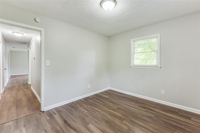 unfurnished room featuring a textured ceiling, baseboards, attic access, and wood finished floors