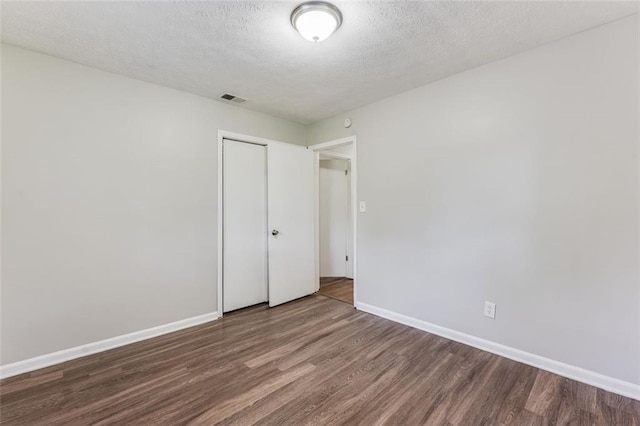 unfurnished bedroom with baseboards, a closet, a textured ceiling, visible vents, and wood finished floors