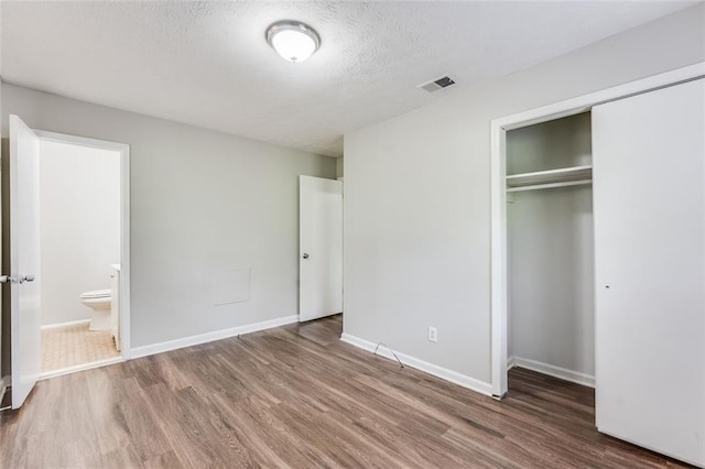 unfurnished bedroom with a textured ceiling, wood finished floors, a closet, and visible vents