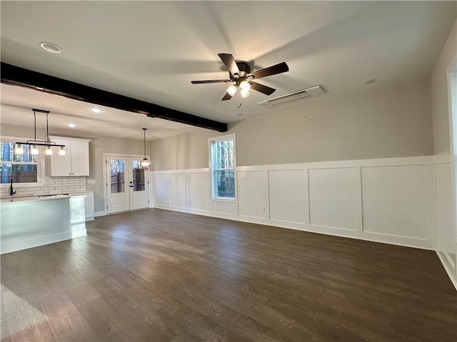 unfurnished living room with beamed ceiling, a healthy amount of sunlight, dark wood finished floors, and a decorative wall