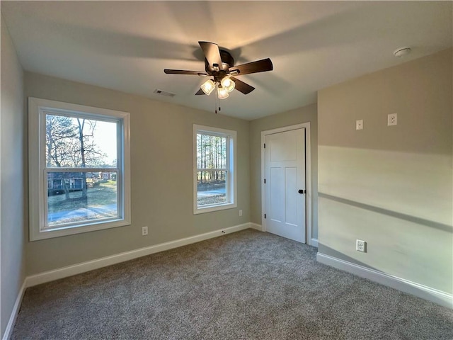 carpeted spare room featuring baseboards, visible vents, and ceiling fan