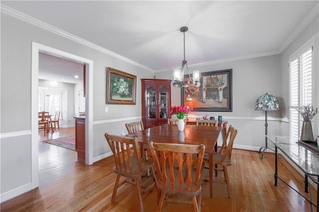 dining area featuring wood finished floors, a chandelier, crown molding, and baseboards