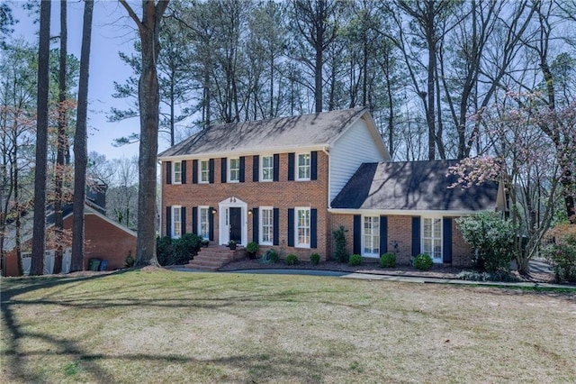 colonial inspired home featuring brick siding, a front yard, and a shingled roof