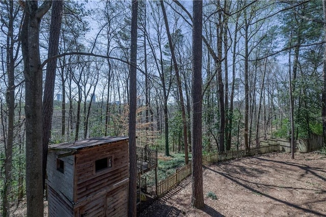 view of yard featuring fence, a wooded view, and an outbuilding