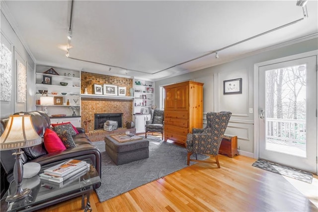 living room featuring track lighting, light wood-type flooring, ornamental molding, built in shelves, and a brick fireplace