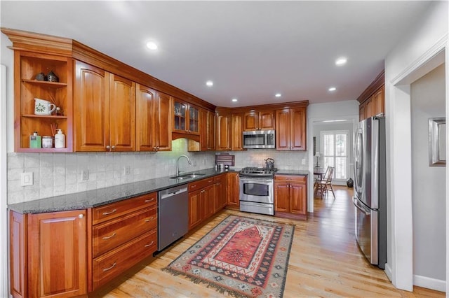 kitchen featuring appliances with stainless steel finishes, a sink, light wood-style flooring, brown cabinetry, and dark stone counters