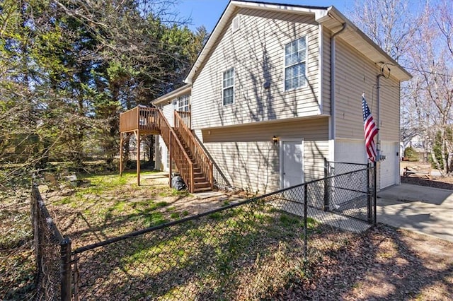 view of side of home featuring concrete driveway, an attached garage, stairs, fence, and a deck