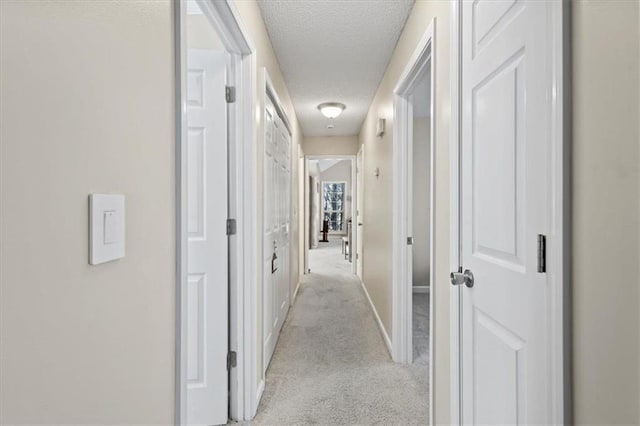 corridor with a textured ceiling, baseboards, and light colored carpet