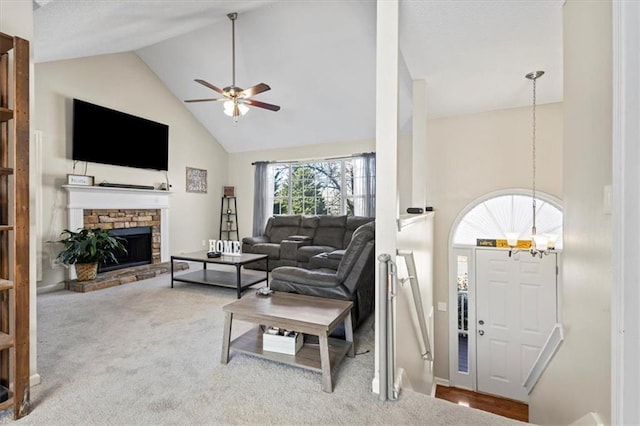 living room with carpet floors, high vaulted ceiling, a stone fireplace, and ceiling fan with notable chandelier