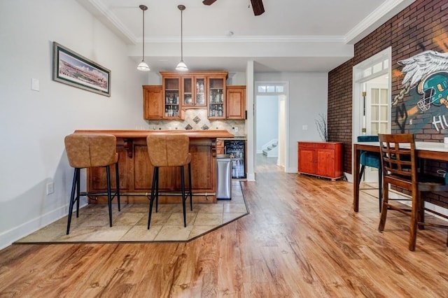 bar with brick wall, decorative light fixtures, tasteful backsplash, ornamental molding, and light hardwood / wood-style flooring