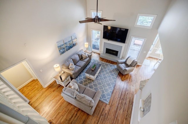 living room featuring hardwood / wood-style floors, a fireplace, ceiling fan, and a high ceiling