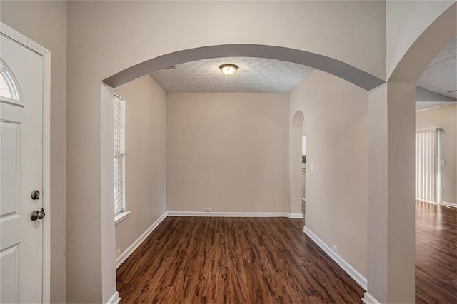 entryway with dark wood finished floors, arched walkways, a textured ceiling, and baseboards