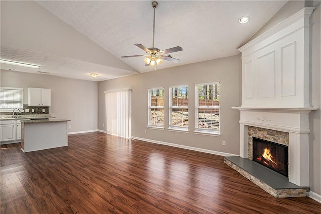 unfurnished living room with a stone fireplace, vaulted ceiling, plenty of natural light, and dark wood-type flooring