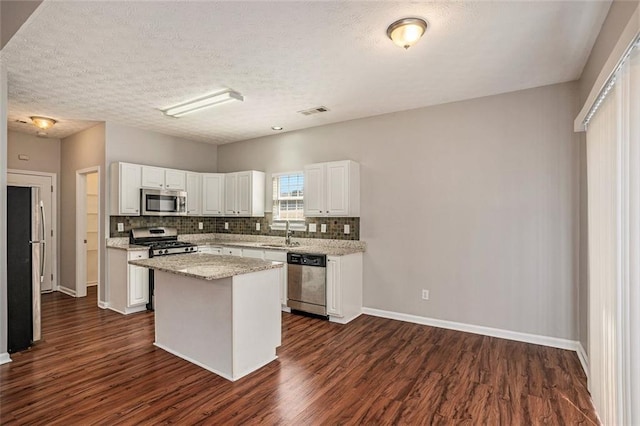 kitchen featuring dark wood-style floors, stainless steel appliances, white cabinets, backsplash, and a center island