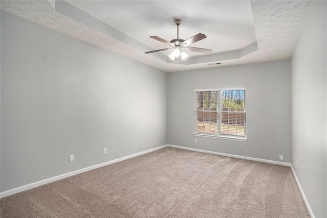 spare room with baseboards, a tray ceiling, carpet floors, a textured ceiling, and a ceiling fan