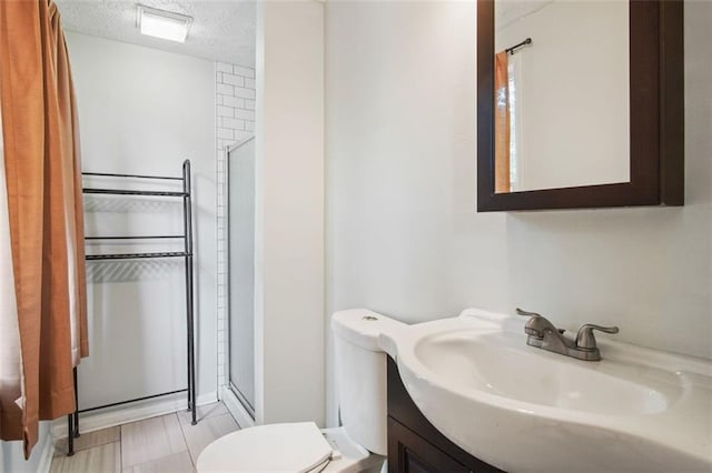 bathroom featuring a shower with door, vanity, toilet, and a textured ceiling