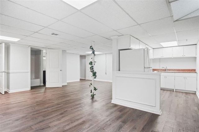 basement with a paneled ceiling, white fridge, dark hardwood / wood-style floors, and sink