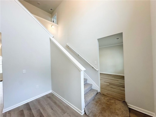 stairs featuring baseboards, visible vents, wood finished floors, and a towering ceiling
