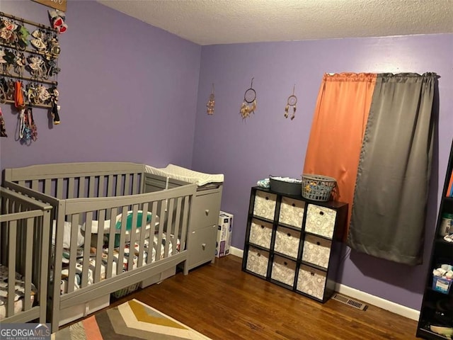 bedroom featuring dark wood-type flooring, a nursery area, and a textured ceiling