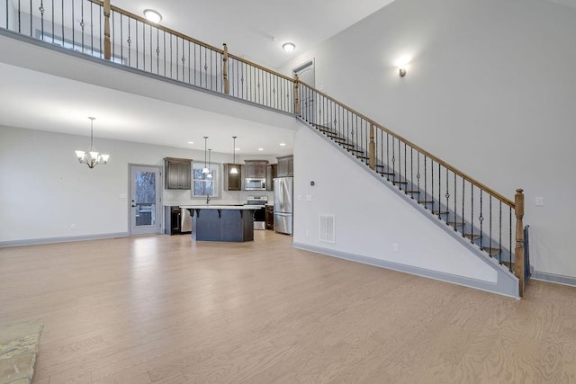 unfurnished living room with a towering ceiling, light hardwood / wood-style flooring, a notable chandelier, and sink