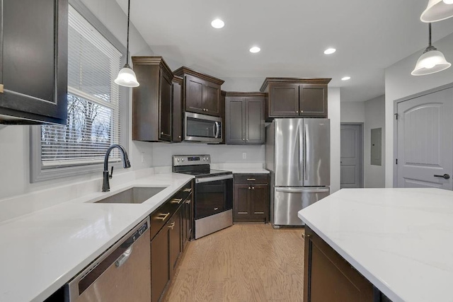 kitchen featuring appliances with stainless steel finishes, light wood-type flooring, dark brown cabinets, sink, and hanging light fixtures