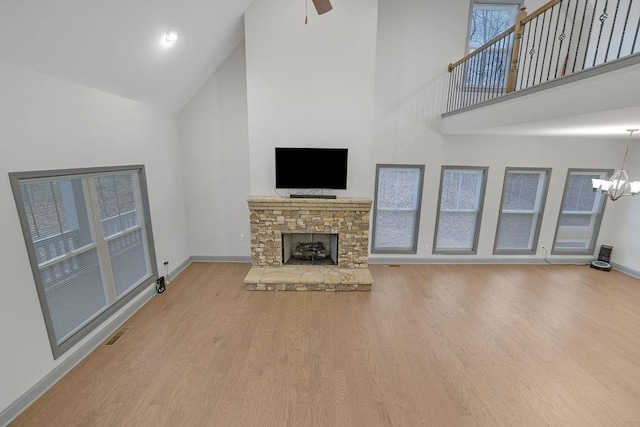 unfurnished living room featuring ceiling fan with notable chandelier, a stone fireplace, light wood-type flooring, and high vaulted ceiling