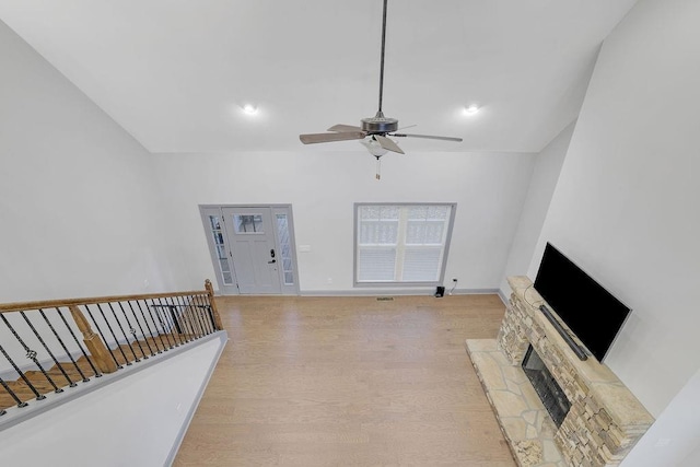 living room featuring a stone fireplace, ceiling fan, and light hardwood / wood-style floors