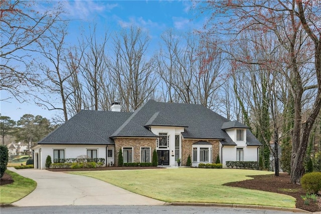 view of front facade with a front yard, driveway, stucco siding, a chimney, and a shingled roof